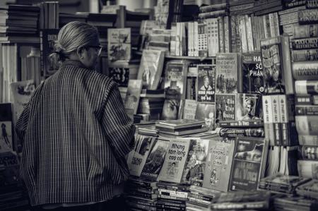 Person Standing in Front of Assorted Books in Gray Scale Photography