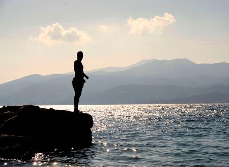 Person Standing on Rock Besides Sea Near Island during Daytime