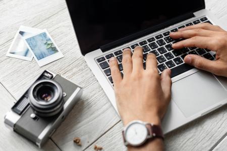 Person Using Macbook Pro Beside Grey Camera on Table