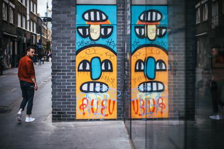 Person Wearing a Red Dress Shirt Walking Near a Wall Graffiti