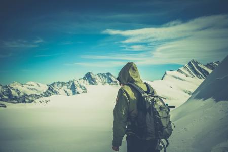 Person Wearing Green Jacket Walking on White Snow Covered Mountain