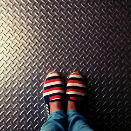 Person Wearing Red-and-multicolored Slip-on Shoes Standing on Gray Metallic Diamond Plate