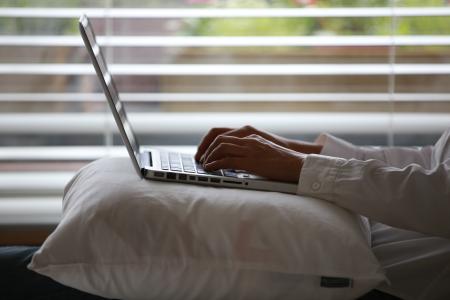 Person Wearing White Dress Shirt Using Silver Laptop on Top of White Throw Pillow