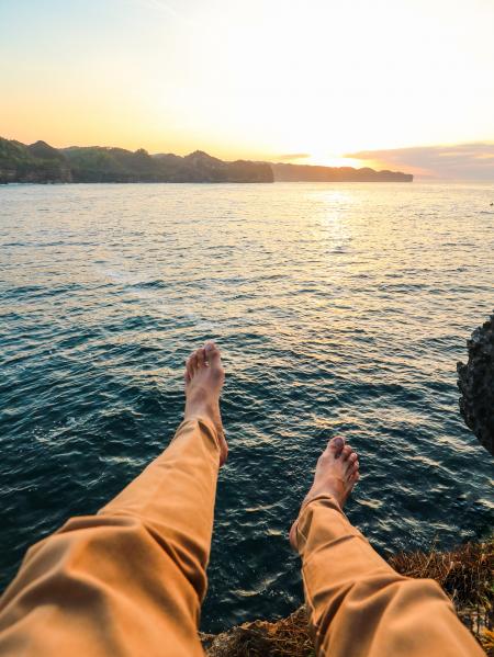 Person Wearing Yellow Pants Sitting on Rock Surrounded by Sea