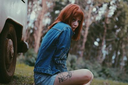 Photo of a Woman in Blue Denim Jacket Sitting Near White Car