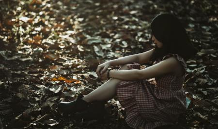 Photo of a Woman Sitting on the Ground Covered with Dried Leaves