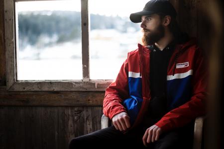 Photo of Man Wearing Black Hat and Blue-and-red Jacket Near Window