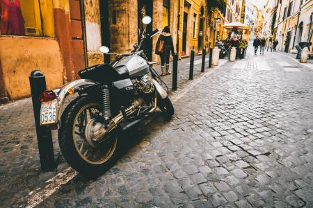 Photograph of Motorcycle Parked Beside Park Bars Near Woman Walking Through Street