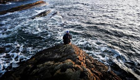 Photography of Person Sitting on Rock Near Ocean