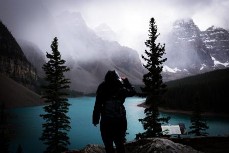 Photography of Person Wearing Coat Standing Between Tall Trees Near River