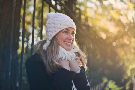 Photography of Woman in Black Jacket and White Knit Cap Smiling Next to Black Metal Fence