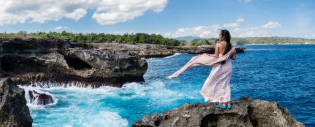 Photography of Woman Standing on Rock in Front of Sea