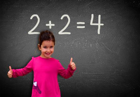 Proud assertive little girl solving a sum on blackboard