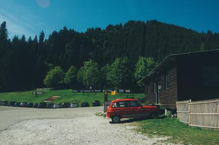 Red 5-door Hatchback Near the Brown Wooden House in Daytime