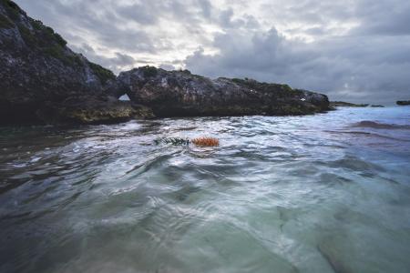 Rocky Cliff Near Calm Sea Under Gray Cloudy Sky