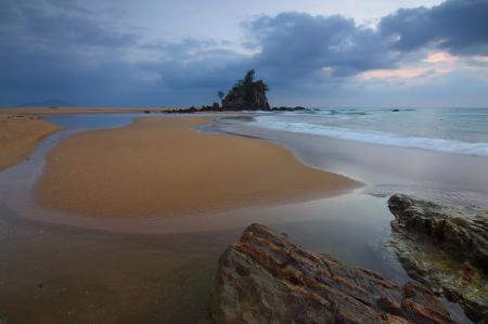 Sea Wave Crashing on Seashore With View of Rock Formation With Trees on Top of It Under Grey Clouds and White Sky