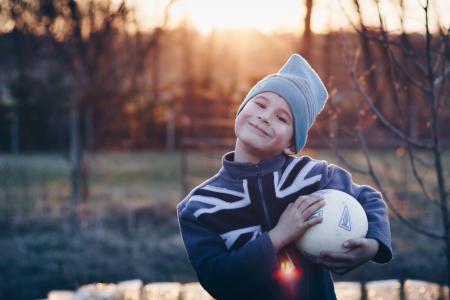 Selective Focus Photography of Boy Wearing Blue United Kingdom Print Zip-up Jacket Carrying White Ball