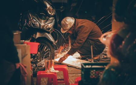 Shallow Focus Photography of Man in Brown Jacket Wearing Gray Hat in Front of Motorcycle