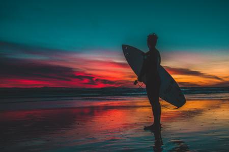 Silhouette of Man in Wet Suit Holding White Surfboard While Standing on Beach during Golden Hour