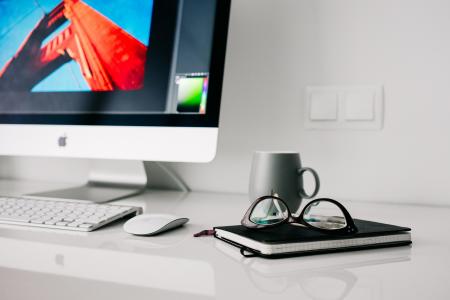 Silver Imac Turned on Beside Gray Ceramic Mug and Black Frame Eyeglasses