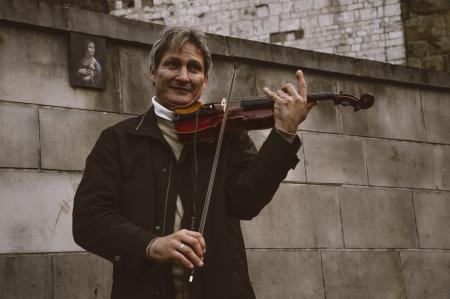 Smiling Standing Man Playing Violin by Gray Stone Wall