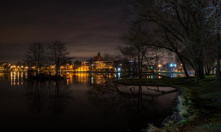 Still Body of Water Next to Lighted Beige Buildings during Nighttime