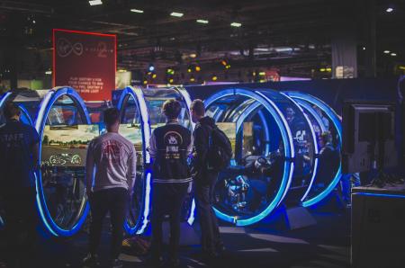 Three Men Standing in Front of Racing Arcade Machines