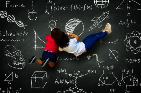 Two little girls writing on a blackboard with science subjects