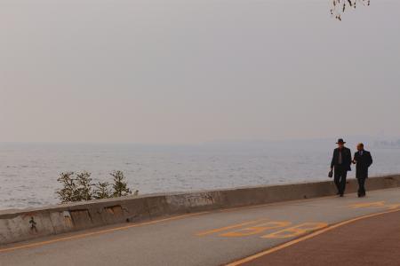 Two Person Walking on a Concrete Road Beside Body of Water