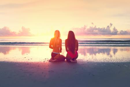 Two Young Women Watching the Sunset Over the Ocean