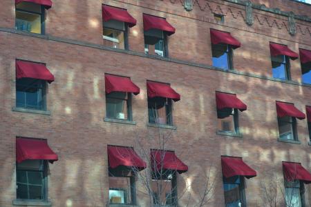 Windows with burgundy canopies along the brick wall of the building