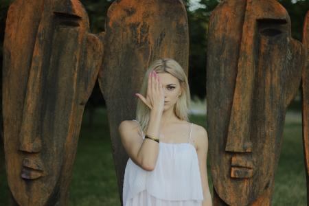 Woman Covering Face With Right Hand in Front of Large Tribal Head Statue