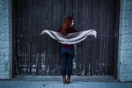 Woman Holding Gray Shawl While Spreading Her Arms Infront of Brown Wooden Door