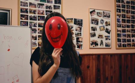 Woman Holding Red Balloon on Her Face Photo Inside Classroom