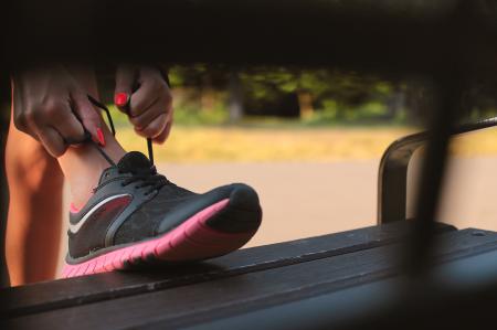 Woman in Black and Pink Sneaker Tying Lace of Her Shoe