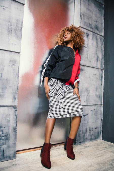 Woman in Black and Red Zip-up Jacket Leaning on Gray Painted Wall