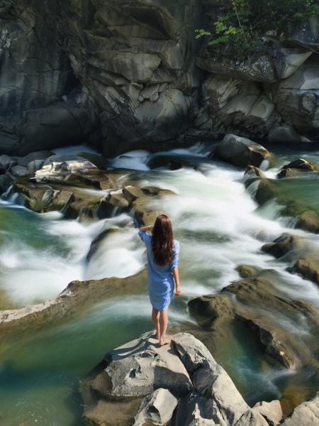 Woman in Blue Long-sleeved Dress Standing in Middle of Rock With Raging Water