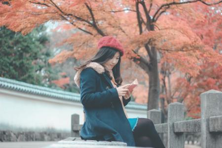 Woman in Blue Parka Jacket Sitting on Grey Concrete Bench Reading Book