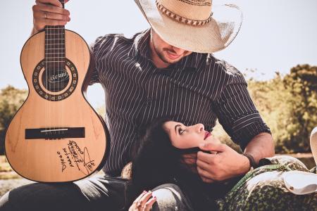 Woman In Green Top With Man In Black Long-sleeved Shirt Holding Autographed Brown Guitar