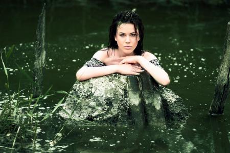 Woman in Grey Shirt in the Water and Leaning Hands on Grey Rock