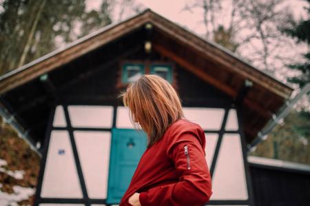 Woman in Red Jacket Standing Near Brown and White Wooden House