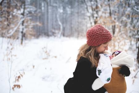 Woman in Red Knitted Cap and Black Top Holding Baby With Brown Carrier