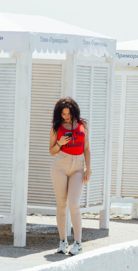 Woman in Red Tank Top and Gray High-waist Jeans Standing Near Wooden Cabinet