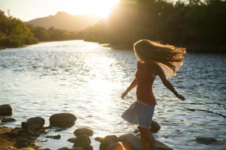 Woman in Red Tank Top Standing on Stone Near Body of Water during Daytime