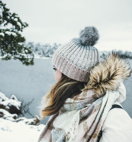 Woman in White and Brown Parka Jacket Wearing Grey Knitted Bobble Hat Near Blue Sea Under White Sky