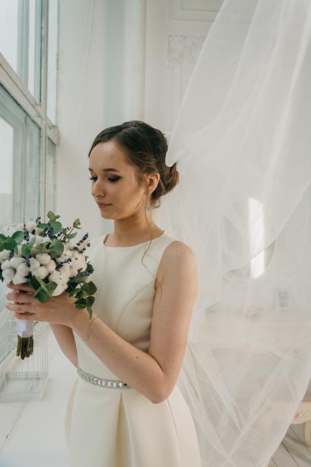 Woman in White Sleeveless Gown Holding White Flower Bouquet Infront of Window