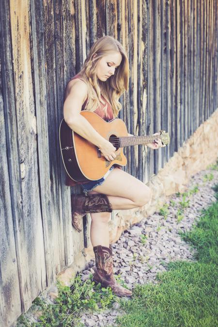 Woman Playing Guitar While Leaning on Wood during Daytime