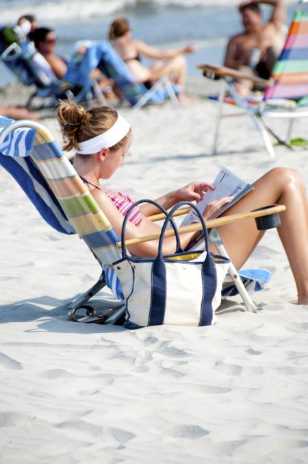 Woman Sitting on the Lounge Chair Reading Magazine on the Beach during Nighttime