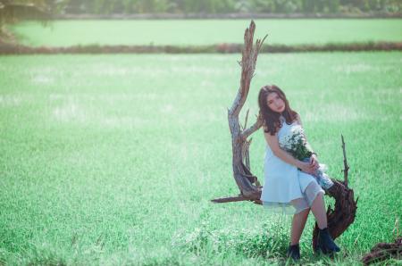 Woman Sitting on Tree While Holding Bouquet of White Flower