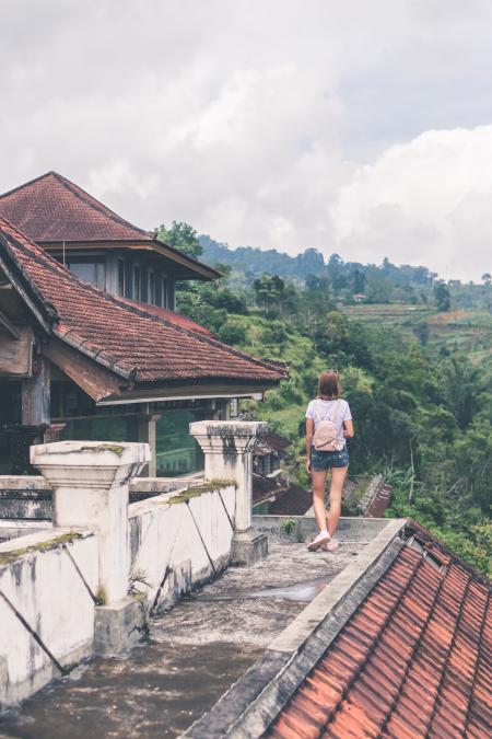 Woman Standing on Gray Concrete Roof Near Mountain Surrounded by Tall Trees